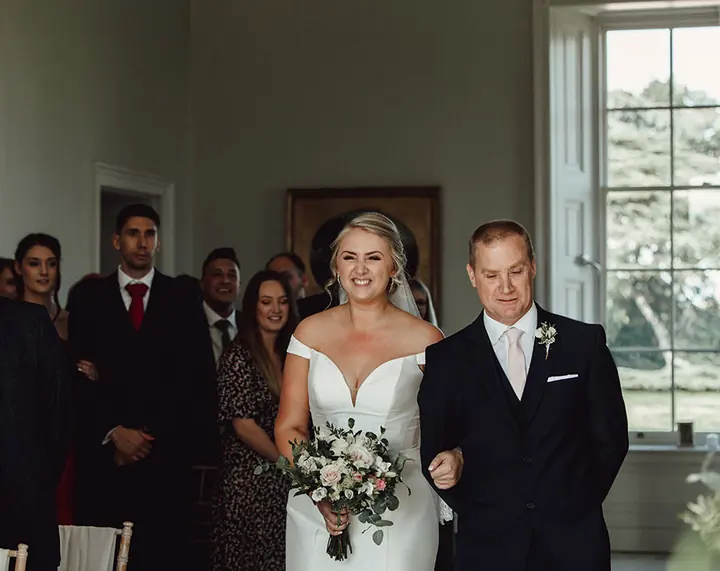 A bride walking in on her father&rsquo;s arm as the guests turn to look
