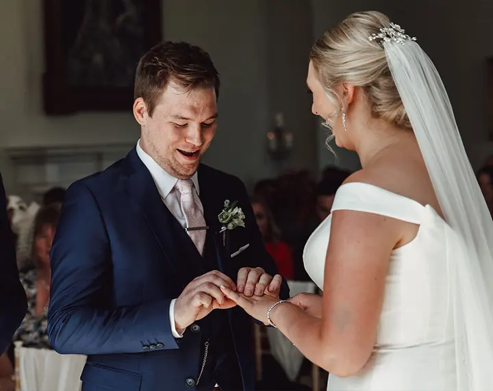 A groom placing the ring on his bride&rsquo;s finger