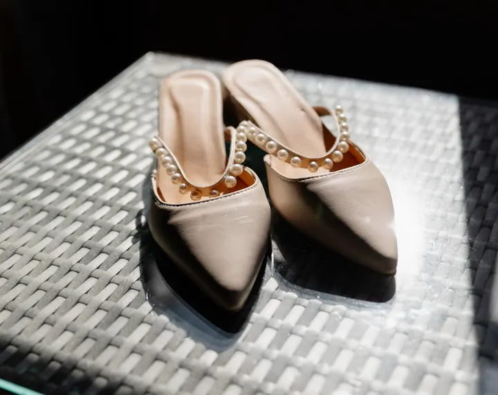 Pearl-trimmed bridal shoes in the sunlight on a woven table