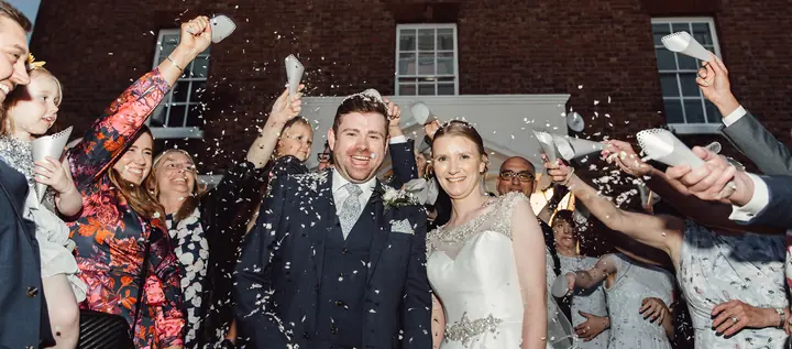 Guests throwing confetti over a couple outside a red-brick house