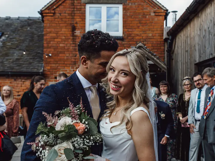 A bride smiling beside her groom as guests gather in a courtyard