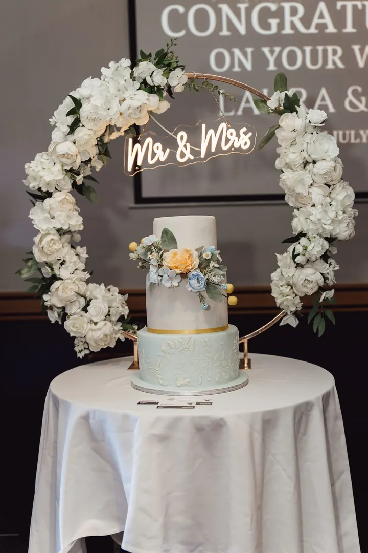 The wedding cake under a floral hoop with a neon Mr & Mrs sign
