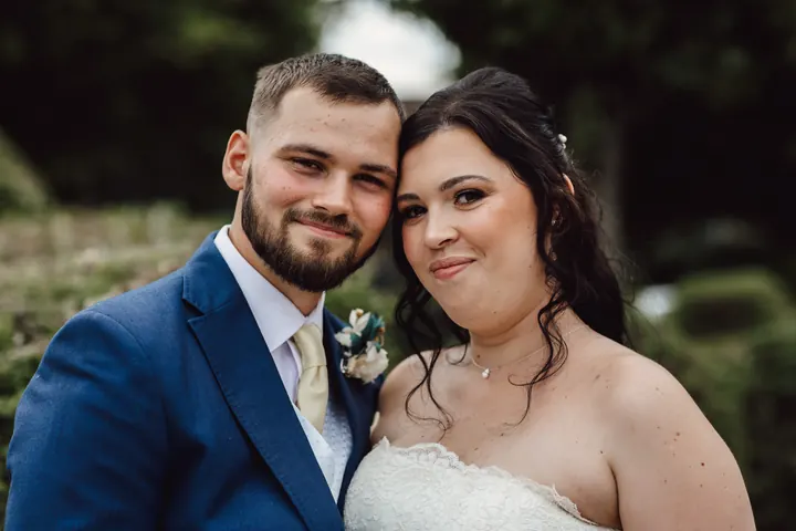 Laura and Owen cheek to cheek in front of the hedges