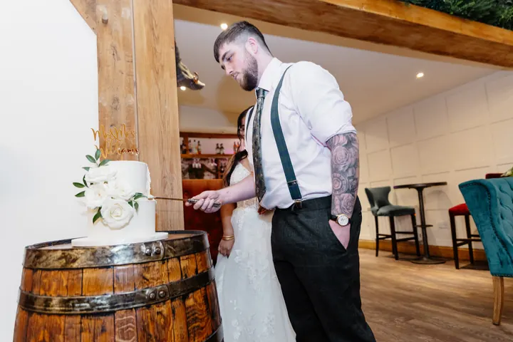 Gloria and Oliver cutting the cake on a barrel