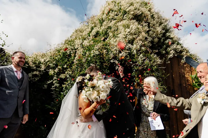 Rose-petal confetti beneath the leafy barn entrance