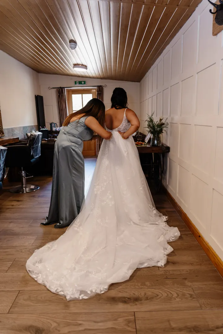A bridesmaid fastening the back of Gloria&rsquo;s dress