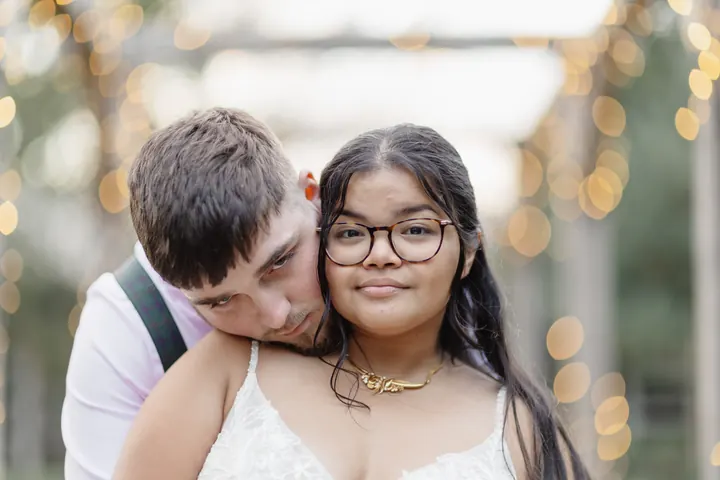 Oliver resting his head on Gloria&rsquo;s shoulder under the fairy lights
