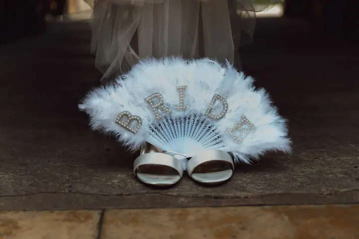 A feathered Bride fan beside bridal shoes