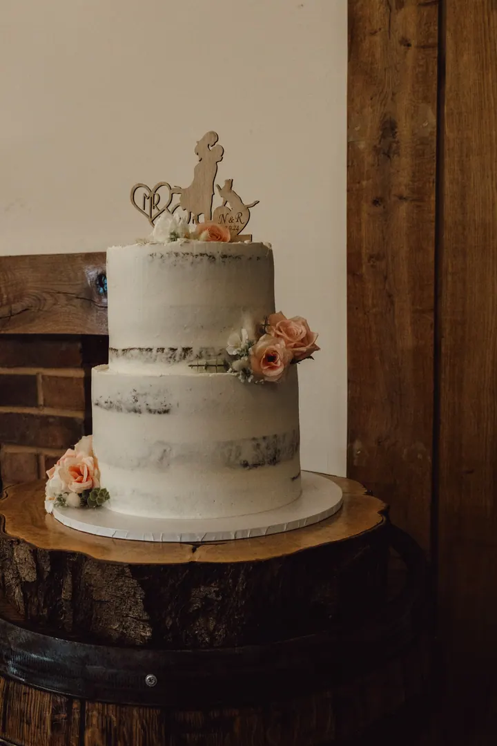 A naked wedding cake with peach roses on an oak barrel