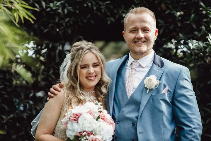 Natasha and Ryan smiling together in front of a hedge