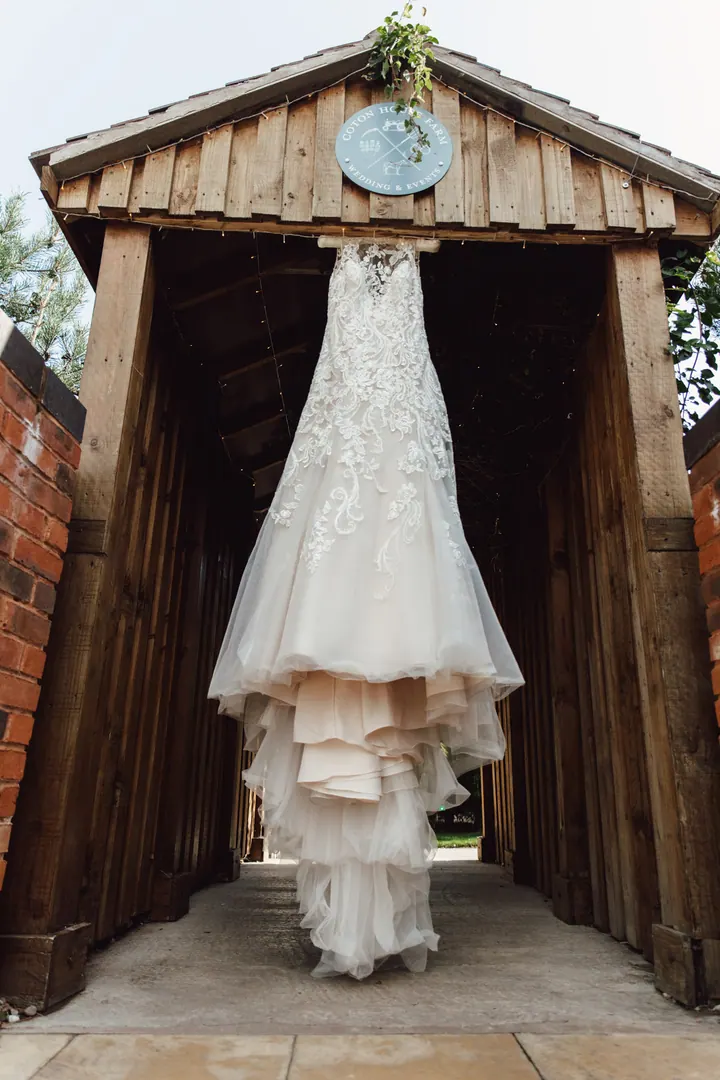 A lace wedding dress hanging in the wooden gateway at Coton House Farm
