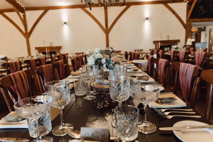 Long dark-wood tables set with crystal glasses and pink chair ties