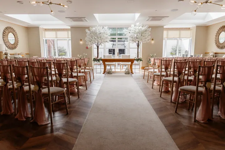 The Garden Room set for the ceremony with white blossom trees and an aisle runner