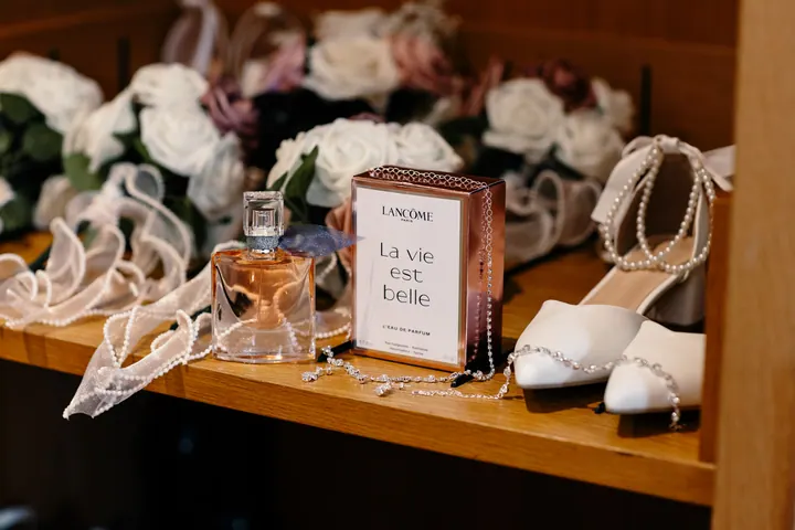 Bouquets, bridal shoes and perfume laid out on a wooden shelf