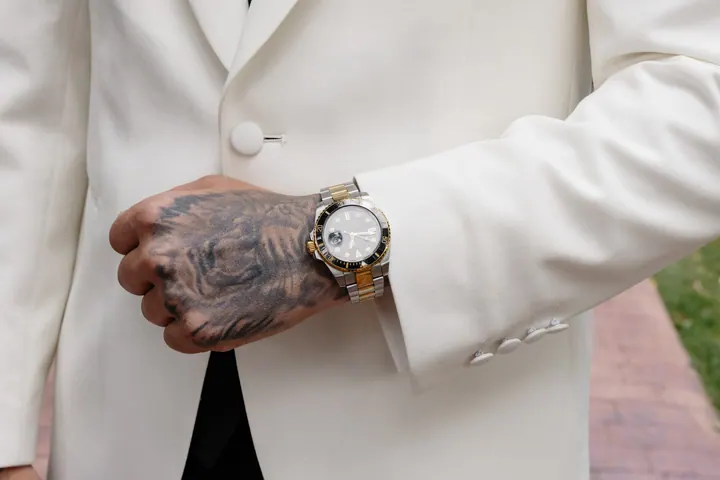 A tattooed hand and watch against a white jacket sleeve