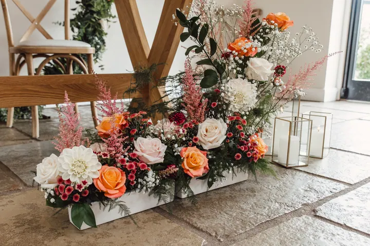 Peach, blush and coral flowers lining the aisle in the ceremony barn