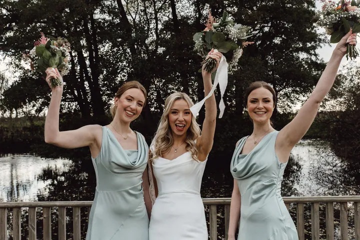 Cicely and her bridesmaids cheering with their bouquets on the deck by the lake