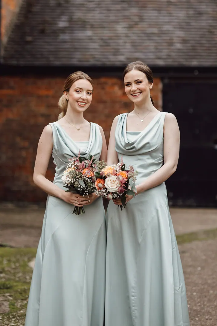 Two bridesmaids in sage green satin with their bouquets