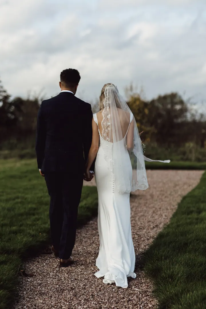 The couple walking away down a gravel path through the gardens