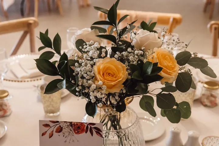 Table centrepiece of yellow and cream roses with eucalyptus