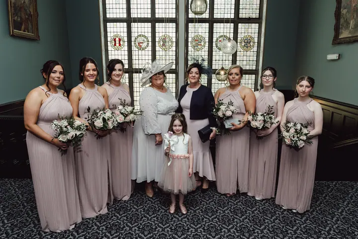 Bridesmaids in blush gowns in front of a stained glass window