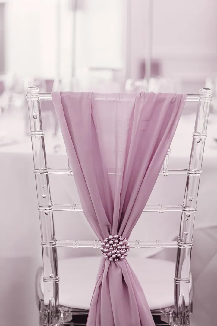 A clear chiavari chair with a blush pink sash