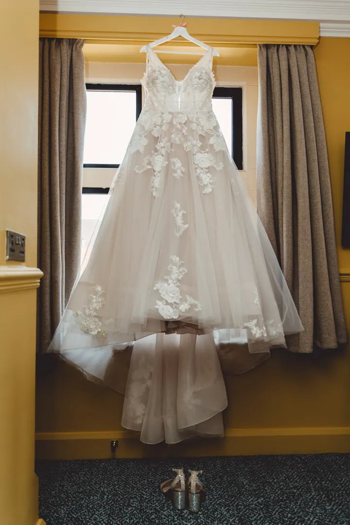 A lace wedding dress hanging in a tall window at Hoar Cross Hall