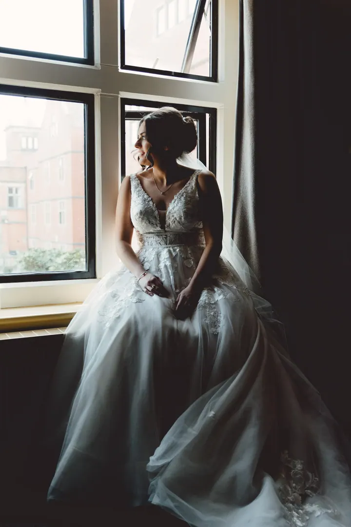 Hannah sitting in a dark window seat in her wedding dress