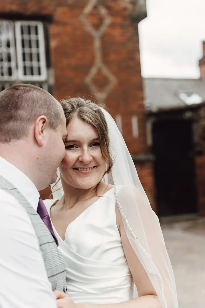 Aleks smiling in Jamie&rsquo;s arms by an old red-brick building