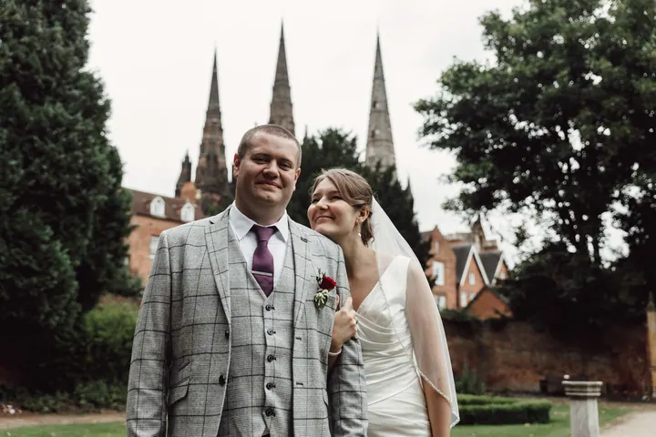 Aleks and Jamie smiling in a garden with the spires in the distance