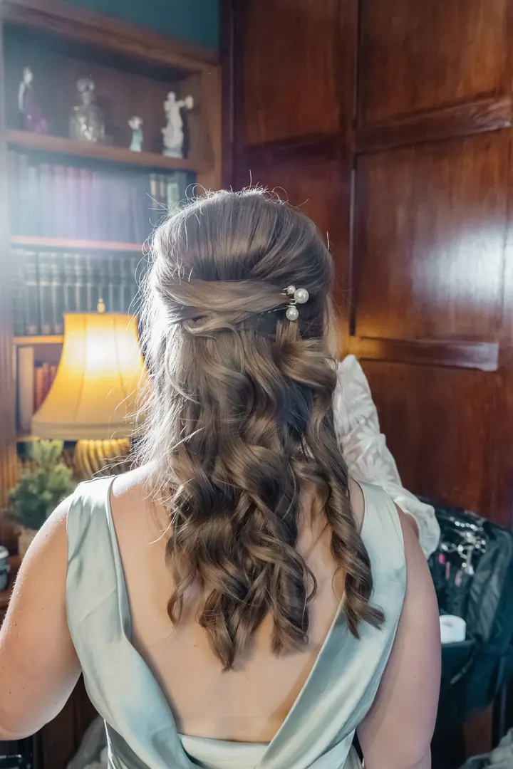 A bridesmaid&rsquo;s curled hair and sage satin dress from behind