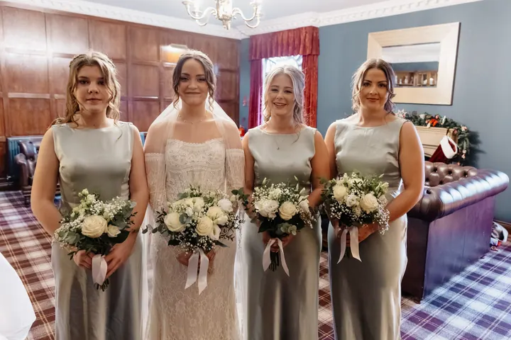 The bridesmaids in sage satin holding white bouquets