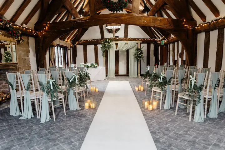 The oak-beamed ceremony room dressed with sage sashes, greenery and candles