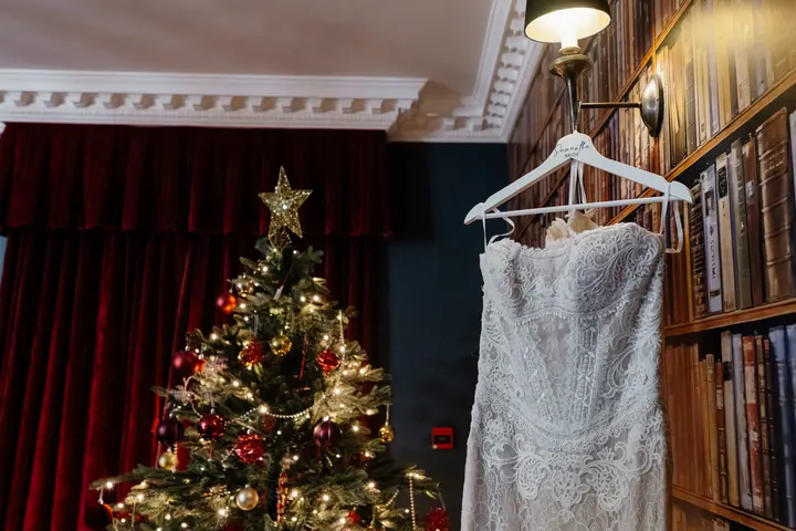 Sam&rsquo;s lace wedding dress hanging beside the Christmas tree in the library at The Moat House