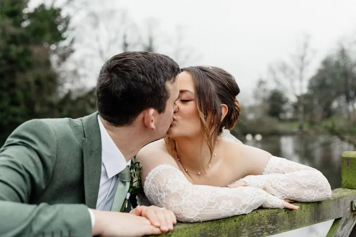 Sam and Andrew leaning on a wooden fence for a kiss