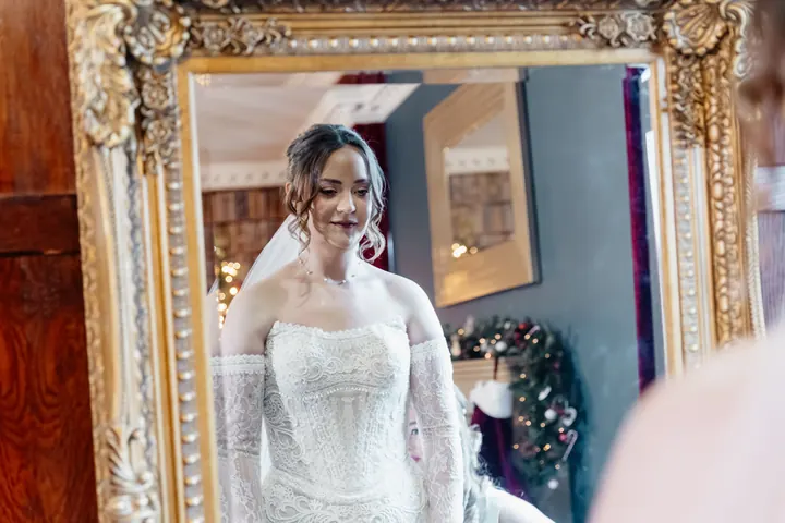 Sam in a gilded mirror as a bridesmaid helps with her veil