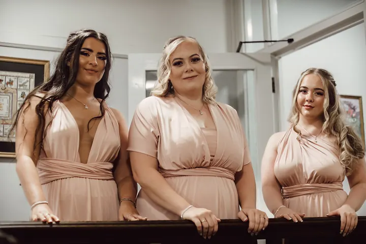 Three bridesmaids in blush pink waiting at the top of the stairs