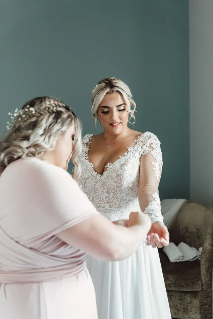 A bridesmaid fastening the back of Sarah&rsquo;s dress