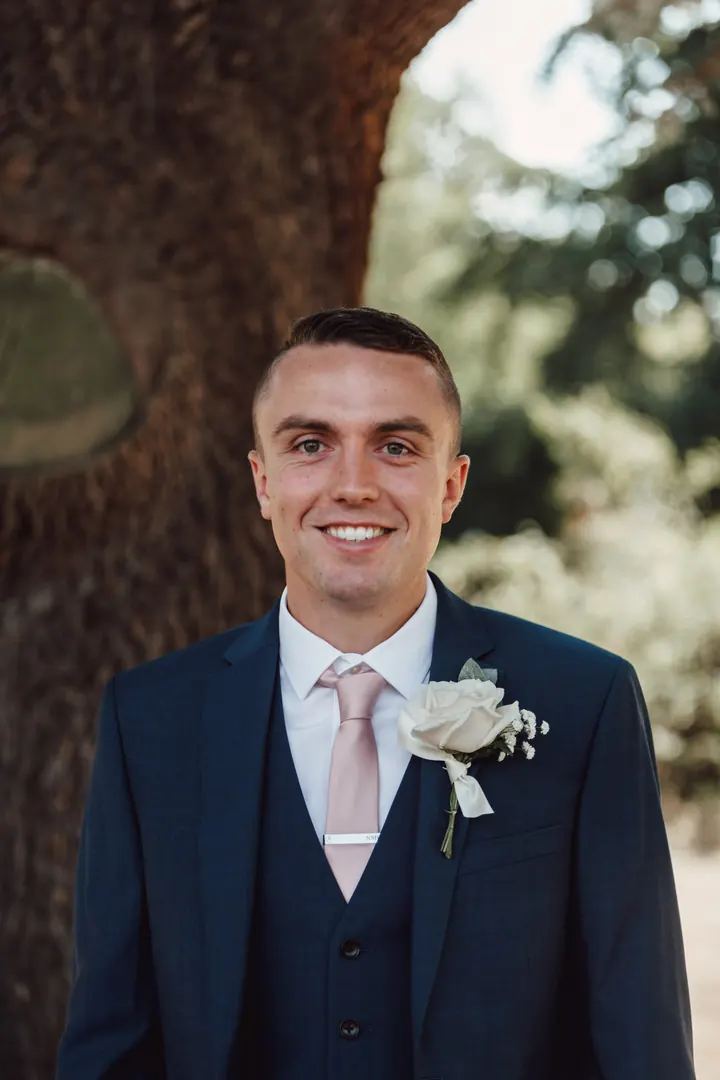 Sam smiling in his navy three-piece suit and blush tie