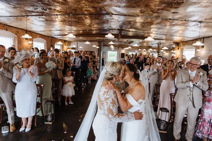The brides sharing their first kiss as guests cheer