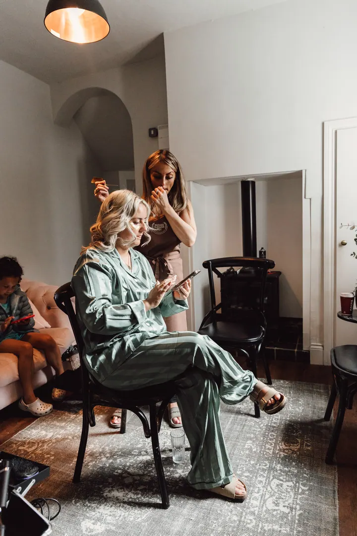 One of the brides in green satin pyjamas having her hair styled