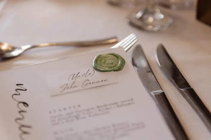 A wedding menu sealed with green wax on a white tablecloth