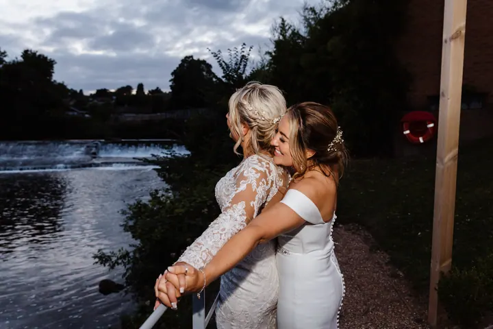 The brides by the river at dusk, one pointing out across the weir