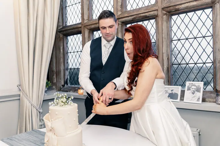 Laura and Darren cutting the cake by the leaded windows