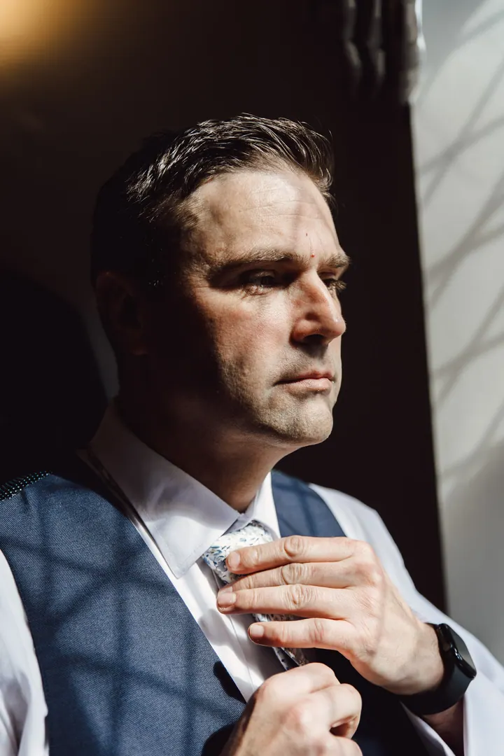 Darren fastening his tie in sunlight through a leaded window