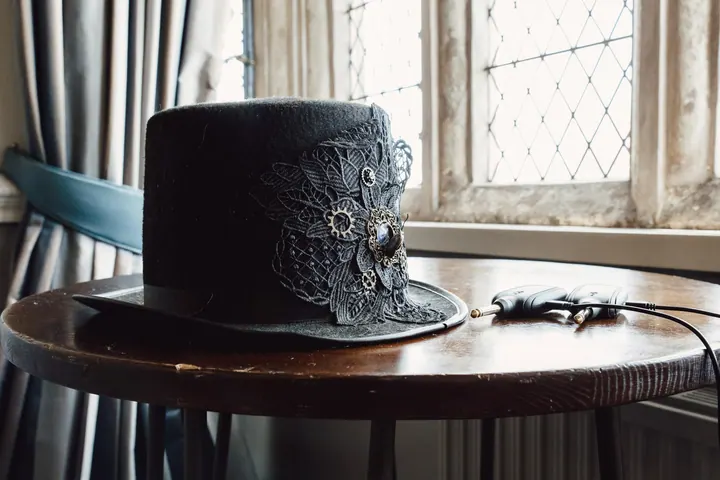 A black top hat on a side table by a leaded window